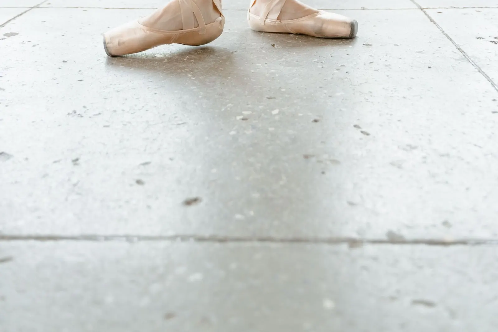 Ballet dancer in black leggings wearing soft pink ballet flats at a barre.